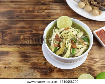 Soto Kudus ayam is a traditional Indonesian chicken soup from Kudus, Central Java. Mainly composed of broth, chicken and vegetables, served in white bowl on the wooden table. Copy space.