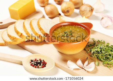 A picture of a bowl of onion soup and its ingredients set on a white table