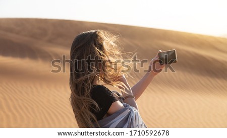 A girl in the desert takes a sunset on the phone A young woman photographs a sunset in the desert on her smartphone.