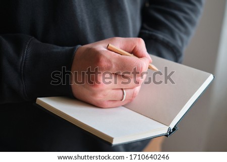 A man makes sketches or notes with a pencil. Writing or drawing on blank paper in notebook. Artist create artwork in sketchbook. Planning a new creative idea. Work on project. Human hands close-up 