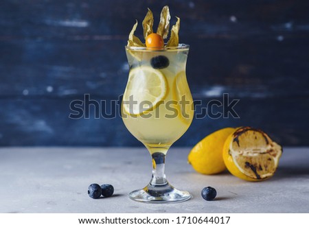 Fresh citrus cocktail with decorations on craft blue background with berries, nuts and greens