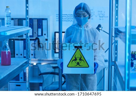 Young woman in protective workwear holding box with chemicals working in the laboratory