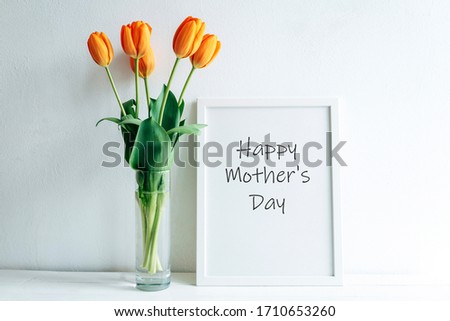 A bouquet of orange tulips in a vase. Frame with a poster Happy Mother's Day. A greeting card.