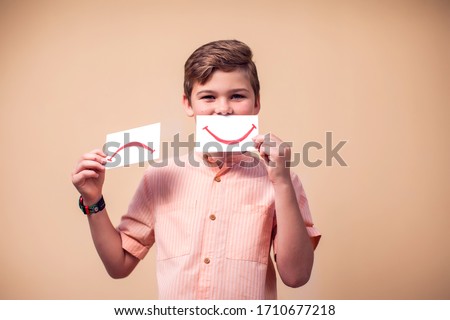 A portrait of kid boy holding positive and negative smile cards. Children and emotions concept