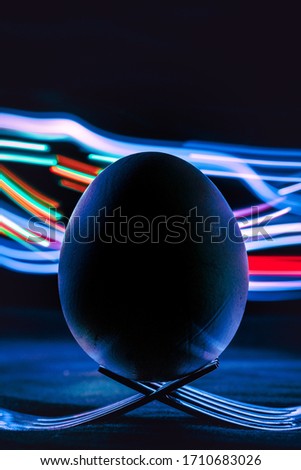 egg with neon light painting on black background supported on fork