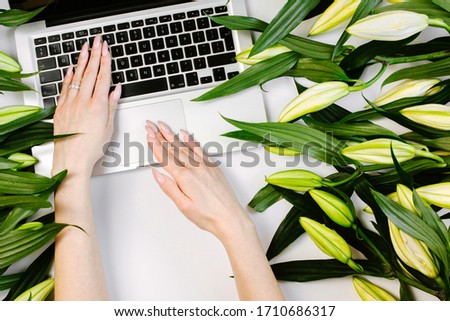 Florist working on a laptop at her beautiful trendy beautiful workspace with laptop and flowers in flat lay style
