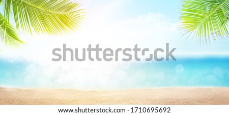 Summer tropical sea with sand beach, palm leaves, sparkling waves and blue sunny sky. Wide template background with copy space