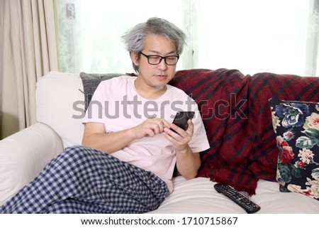 The Asian man using smart-phone in the livingroom.