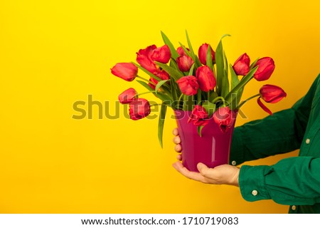 man holds a vase in his hands with a bouquet of red tulips. Delivery of flowers and gifts for mother's day and birthday. Place stinging text. Studio bright eelt background. copy-space