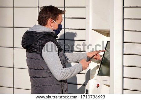 Young man in a blue mask picks up a package at Boxes for parcels. Contactless or non-contact delivery of goods and products during coronavirus epidemic or pandemic.Self-service, quarantine Royalty-Free Stock Photo #1710736693