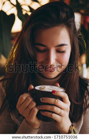 woman with exquisite smile and beautiful eyes having breakfast with her friend in a cozy cafe. She drinks latte sitting in a chair at a table