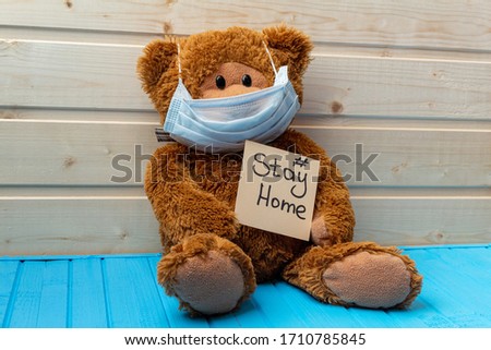 teddy bear with words stay at home in protective medical mask on the wooden background