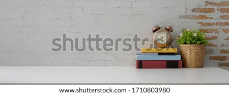Close up view of contemporary workspace with books, decorations and copy space on white table with brick wall