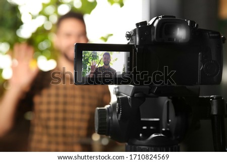 Young blogger recording video indoors, focus on camera screen
