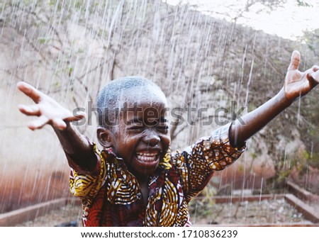 Candid Photo of cheerful African Black Boy So Unbelievably Happy to get Water from Rain in Dry Season