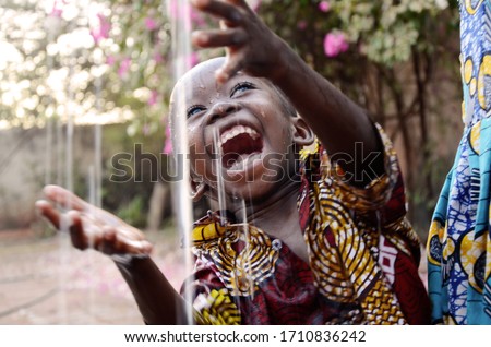 Unbelievably happy African baby child enjoying the raindrops from his roof top in his house in Bamako, Mali.