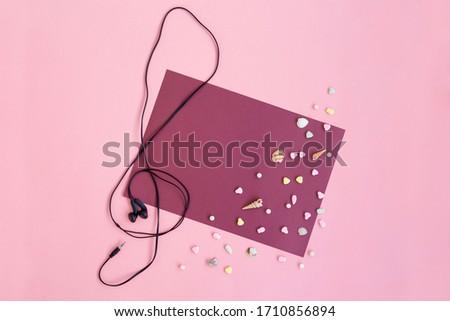 The concept of beautiful music: a treble clef composed of earphones on a pink and beard background with multi-colored sweets and shells