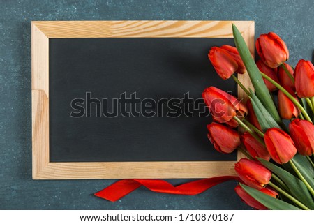 Red tulips and chalkboard on the blue background, blank for a postcard for the teacher's day. Copy space.