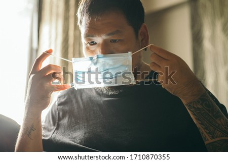 Asian man putting protective mask on his face in the house. Concept about Corona Virus.