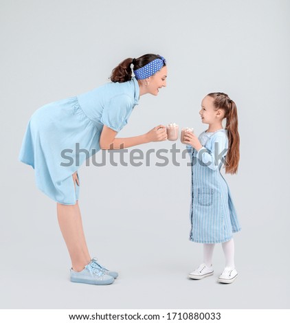 Woman and her little daughter with tasty cocoa drink on light background