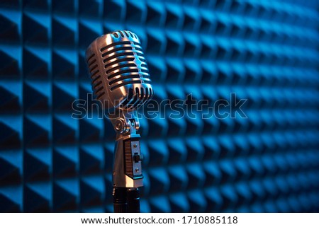Studio retro condenser microphone on acoustic foam panel background with blue side light, copy space on right