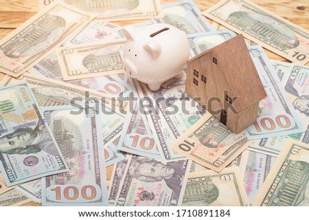 wooden home model with piggy bank and many dollar bank on the table, saving money for buy property.