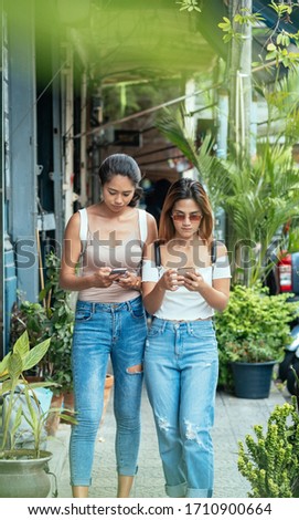 Two friends looking into smartphones while walking on city street stock photo