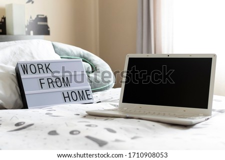 Zenithal picture of a light box with a message and a laptop with black screen on a bed in a bright bedroom.Work from home message.