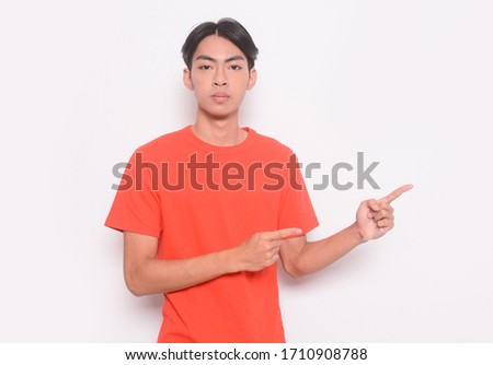 Young handsome elegant man wearing orange t-shirts with two hands and fingers to the side
