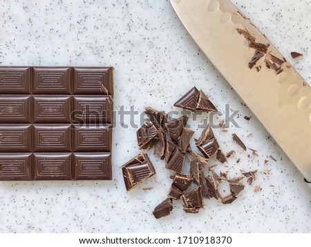 Topdown closeup view of a block of dark chocolate cut with knife on a cutting board. The chocolate is cut into small bite sized bits and pieces. Royalty-Free Stock Photo #1710918370
