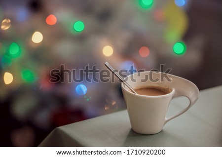 beautiful white cup with cocoa on a table with a laptop on a background of lights evening romantic picture