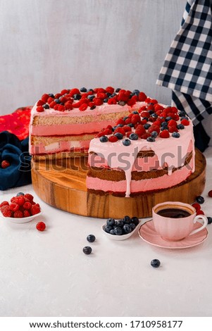 Cream berry cake with raspberry and blueberry with a slice cut out on wooden board on the table background with coffee cup. 