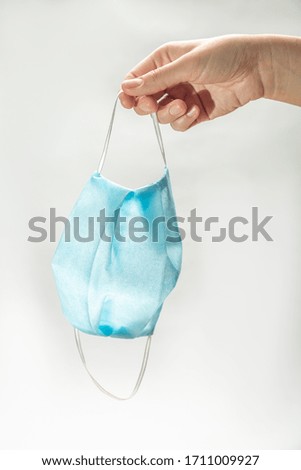 hand holding in fingers a blue disposable medical mask on weight on a white background. vertical orientation