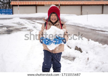 Portrait of happy little Asian boy holding a snow ball, having fun in a winter park.