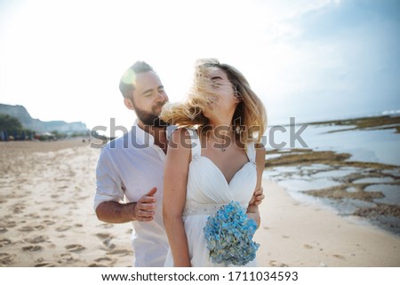 couple in love - bride and groom with a blue bouquet on the wedding day hug and kiss on the beach by the ocean on the exotic Asian island of Bali in Indonesia, incredible landscape Royalty-Free Stock Photo #1711034593