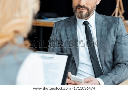 Selective focus of businessman using smartphone near businesswoman with contract in office