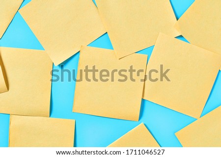 Scattered many yellow square blank paper stickers on blue background. Copy space. Top view