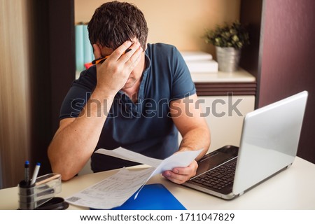 The shocked and disappointed man saw the bad news in the invoices. Frustrated unemployed man with documents.  Royalty-Free Stock Photo #1711047829