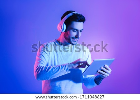 Modern gadgets for joy concept. Happy man in wireless headphones uses tablet Royalty-Free Stock Photo #1711048627