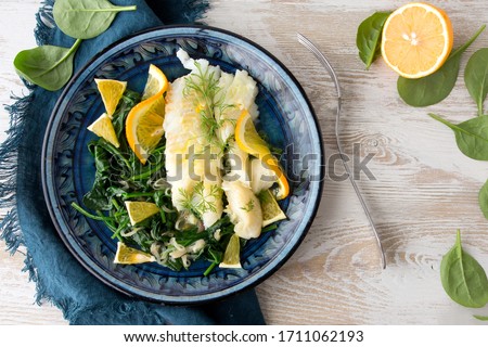 halibut fillet with spinach garnish and orange sauce on a blue ceramic plate on a light wooden table