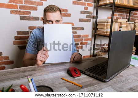 Young male businessman working remotely, holding a piece of paper and looking through it