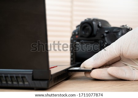 The photographer's hand captures memory. card black dlsr digital camera inserted in the slot of the laptop