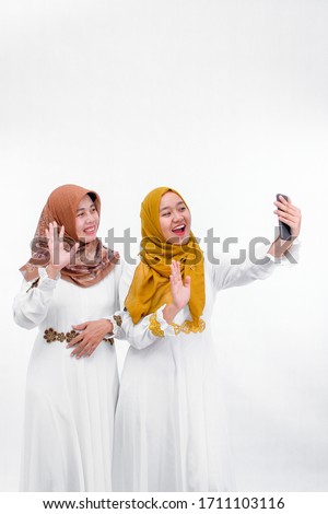 two muslim woman wear hijabi taking video calling with smartphone isolated over white background, ramadan celebration concept
