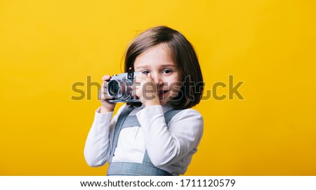 Portrait of a girl using a photo camera on yellow background. Pic with copy space.