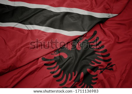 waving colorful flag of albania and national flag of trinidad and tobago. macro
