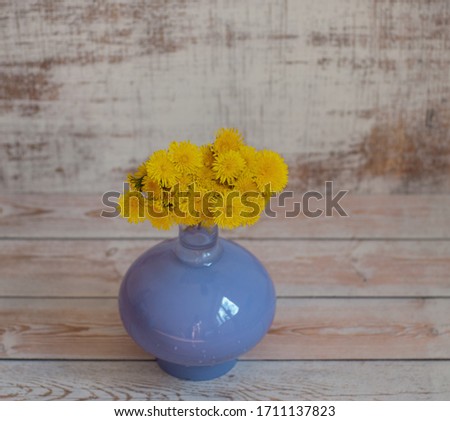 Yellow bouquet of dandelion flowers in a purple glass vase on a light background. A beautiful curved vase with flowers. Yellow-purple. Plants.