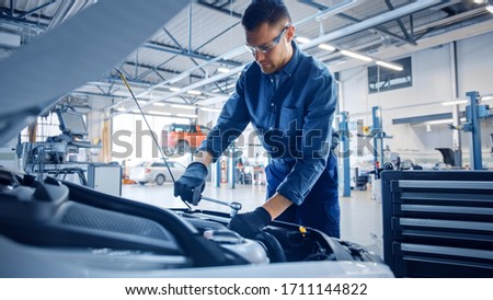 Professional Mechanic is Working on a Car in a Car Service. Repairman in Safety Glasses is Fixing the Engine on a Vehicle. Specialist Unscrews Bolts with a Ratchet. Modern Clean Workshop. Royalty-Free Stock Photo #1711144822