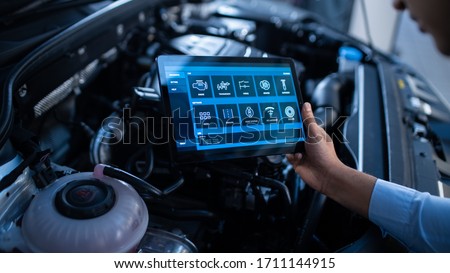 Car Service Manager or Mechanic Uses a Tablet Computer with a Futuristic Interactive Diagnostics Software. Specialist Inspecting the Vehicle in Order to Find Broken Components In the Engine Bay. Royalty-Free Stock Photo #1711144915