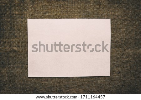 Empty white horizontal rectangle poster mockup with soft shadow on darkened burlap background. Flat lay, top view