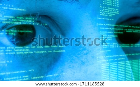 The eyes of a woman (a computer programmer) looking at the camera, with source code (program instructions) projected over her face. Blue tones, green characters.
